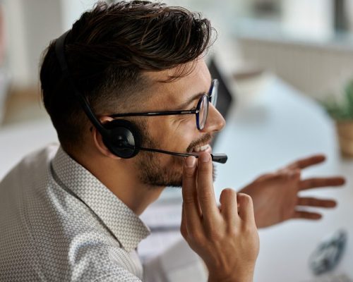 Happy call center agent wearing headset while talking with clients and working in the office.